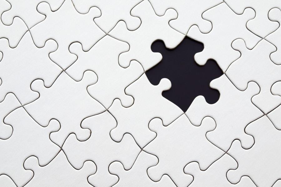 A missing puzzle piece among a completed white puzzle