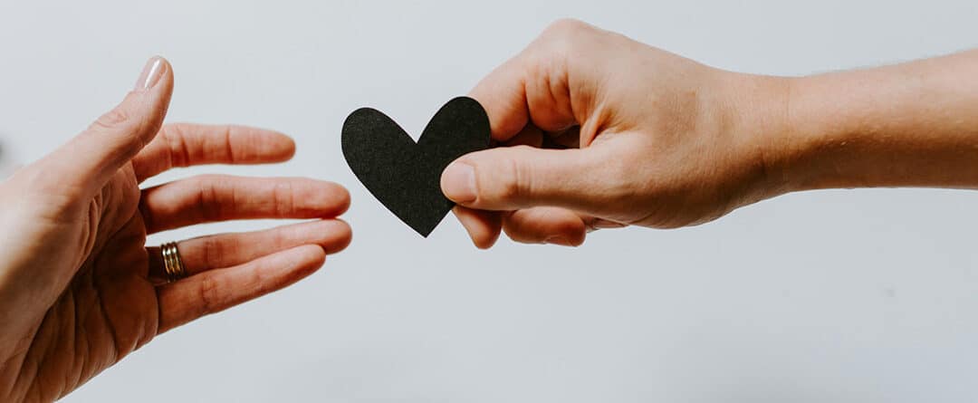 A hand holds out a paper heart to another hand